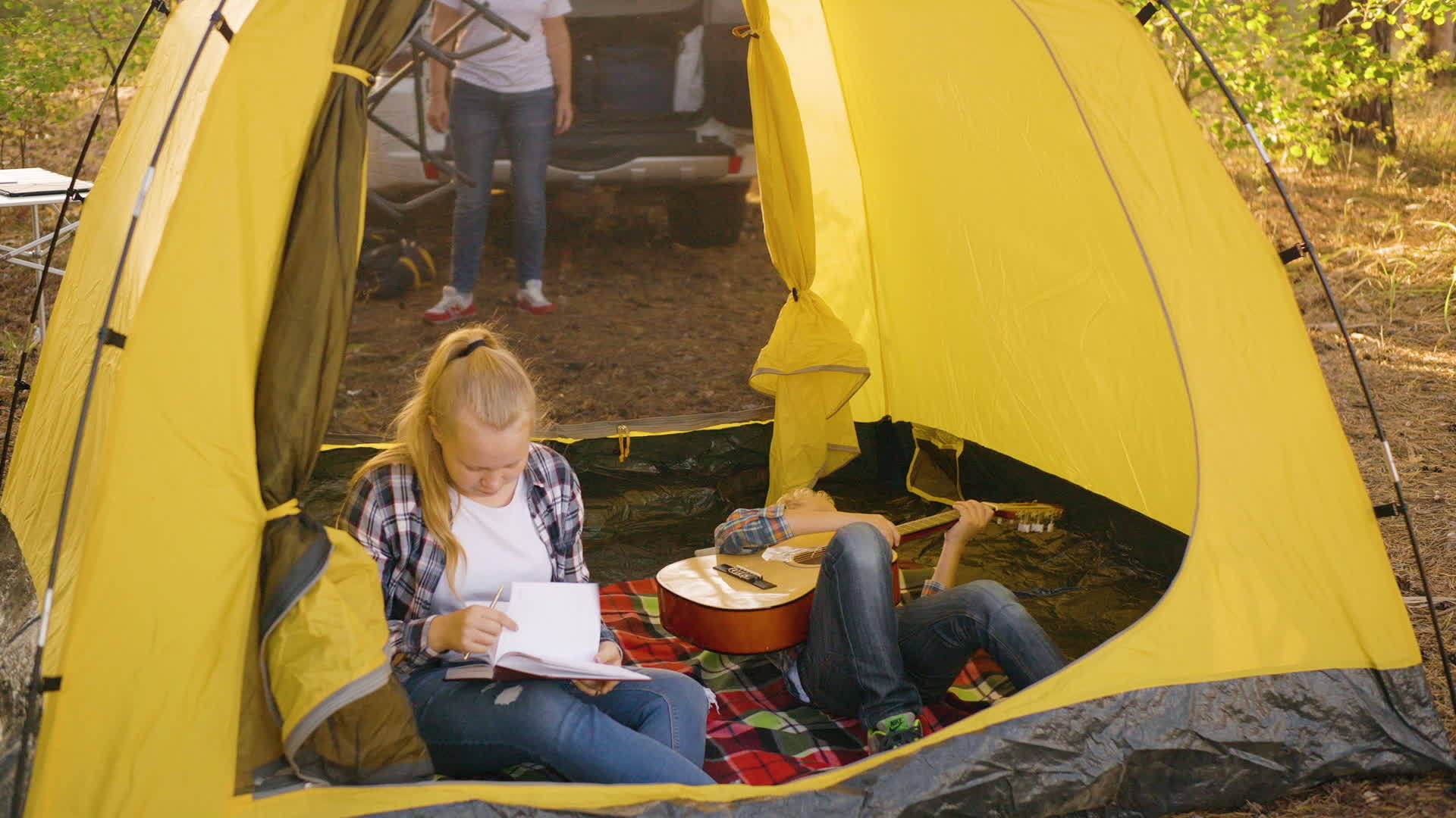 女孩检查笔记本男孩玩吉他的露营地视频的预览图