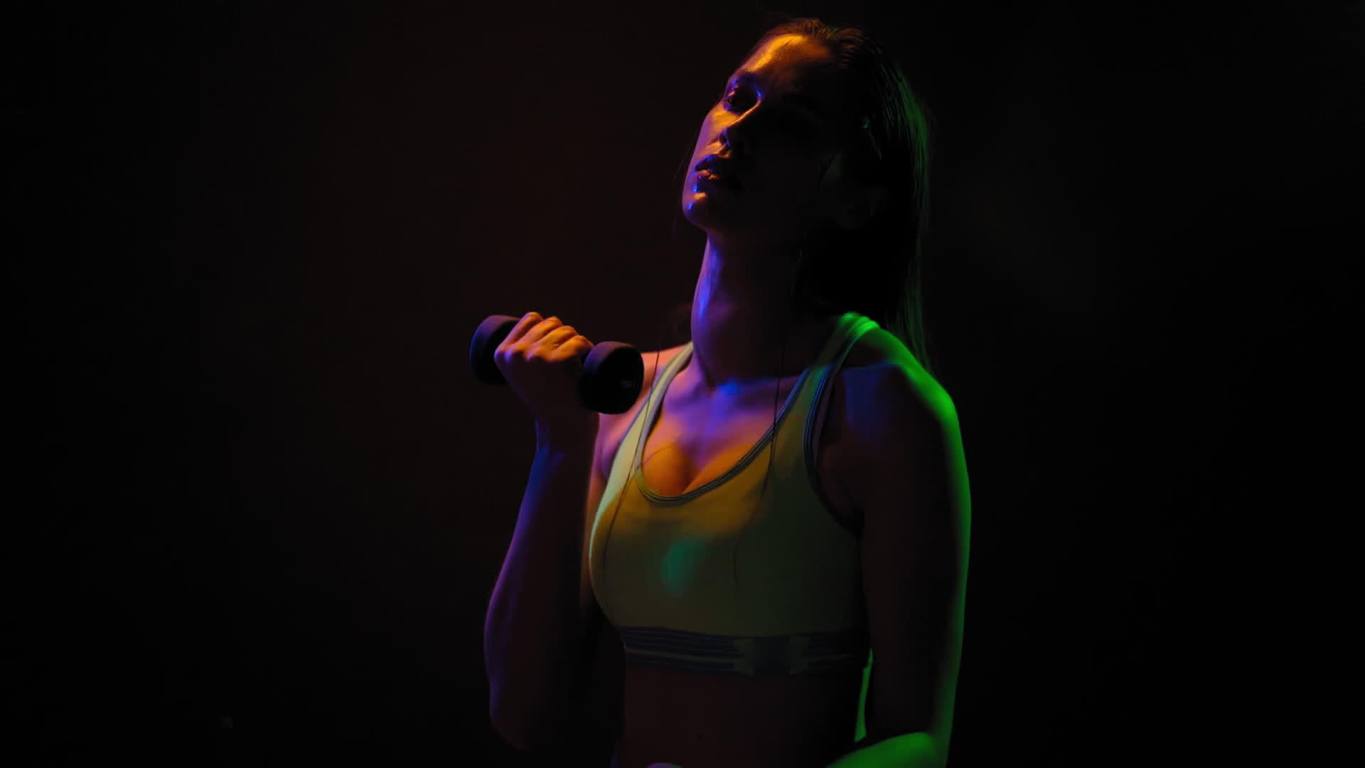 美丽的女孩摆姿势锻炼二头肌哑铃站在霓虹灯下视频的预览图