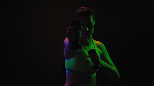 健身女孩在霓虹灯下用哑铃锻炼她穿着运动夹克伸展颈部肌肉视频的预览图
