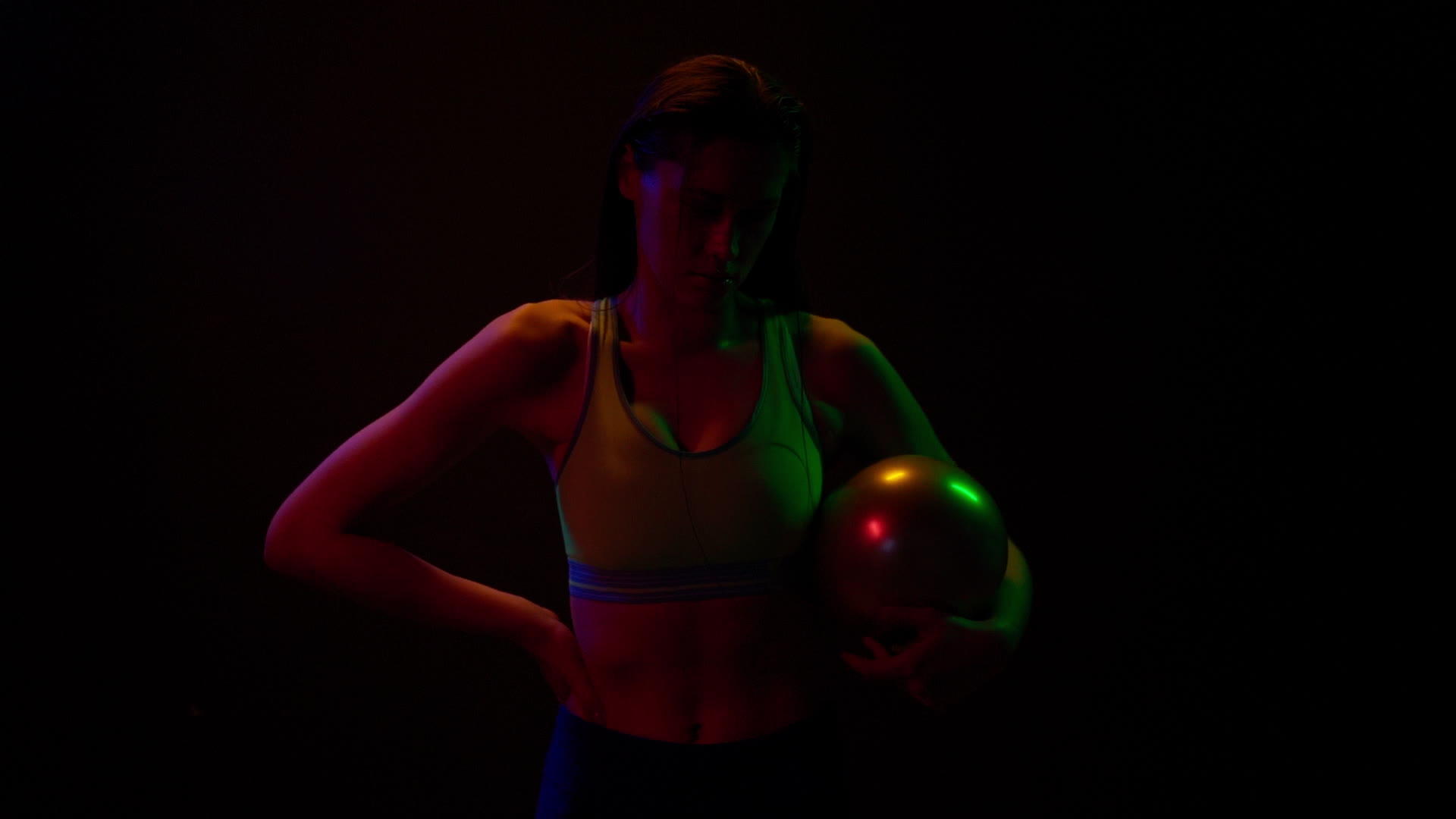美丽的女孩手里拿着一个球站在霓虹灯下穿着运动夹克伸展视频的预览图