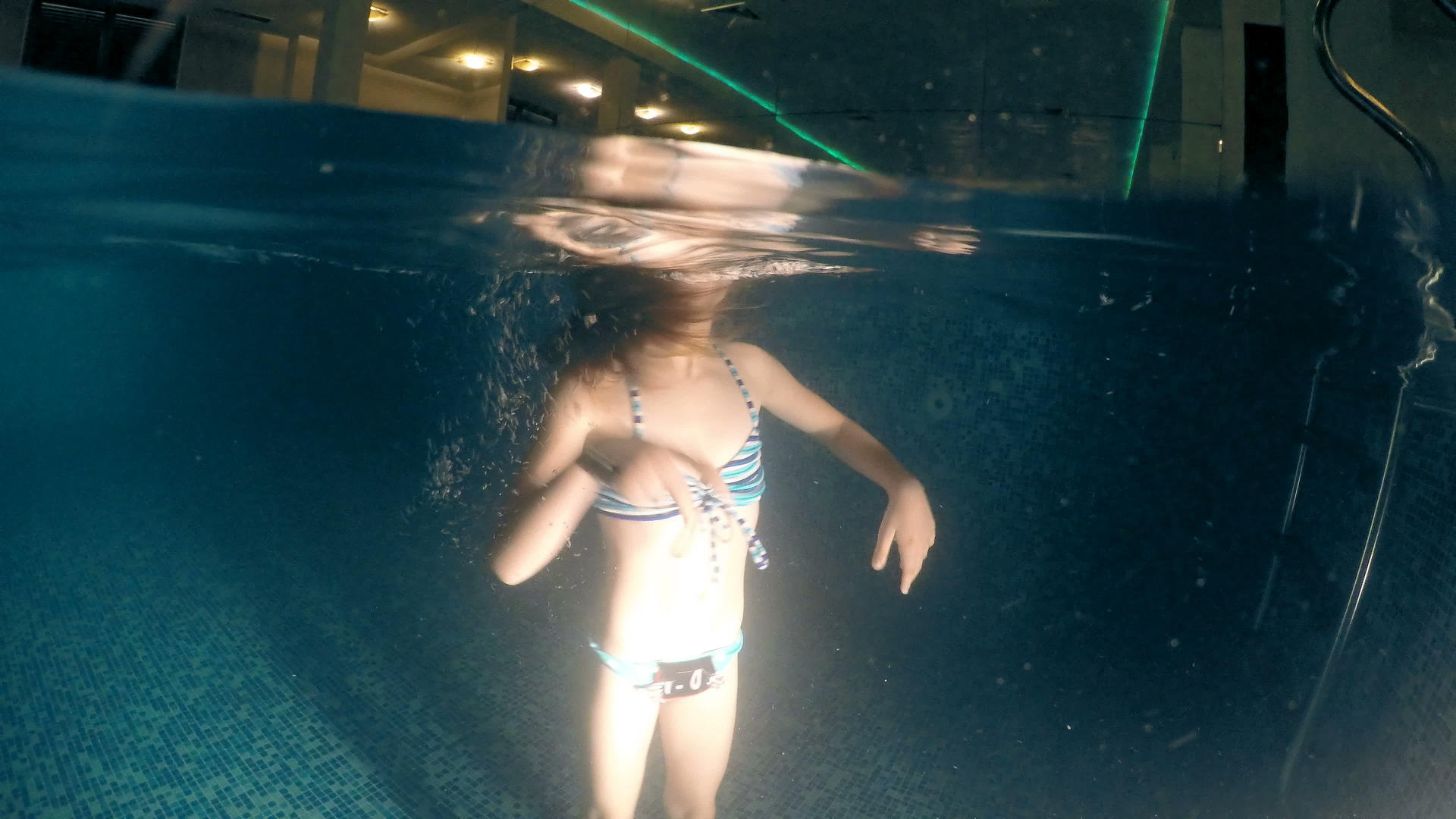 小女孩在水下玩得很开心在黑暗的豪华游泳池里转身视频的预览图