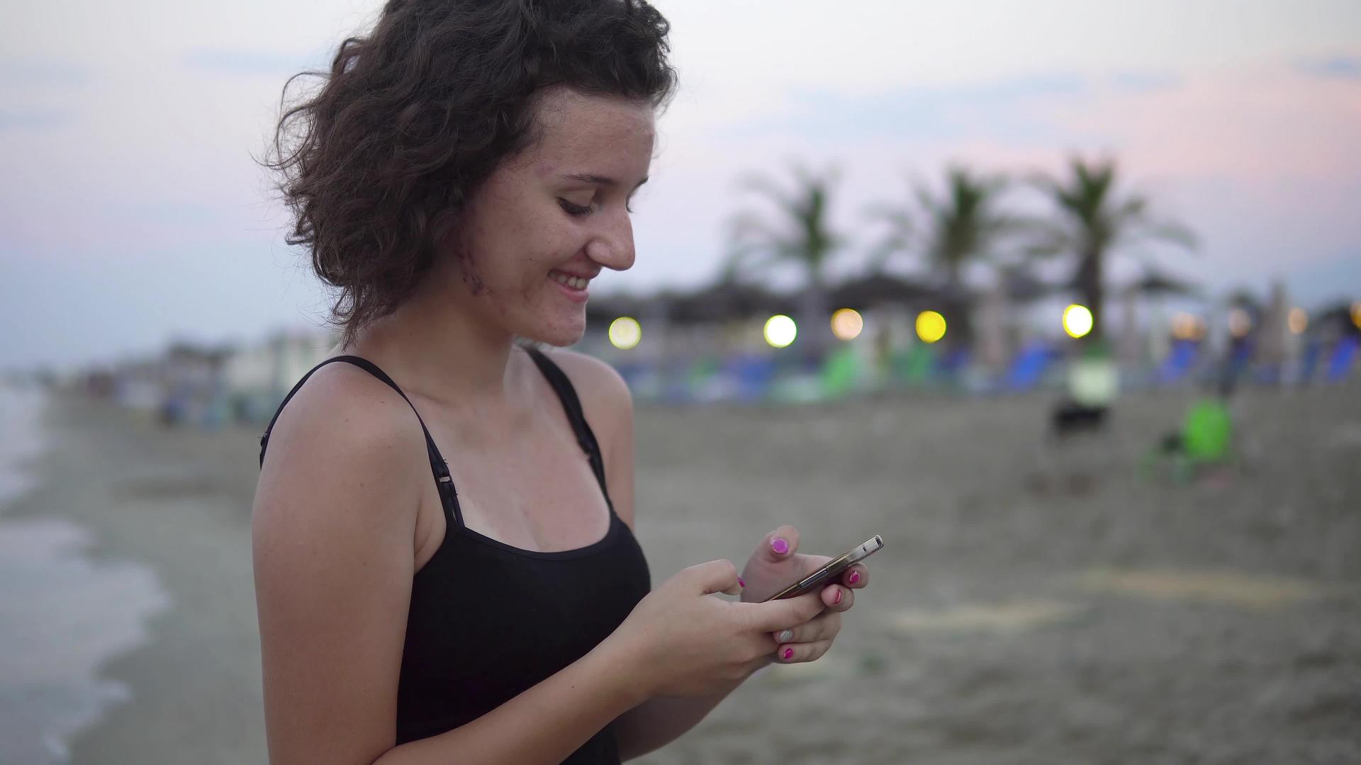 可爱的女孩在她的智能手机上发短信在空海滩上笑视频的预览图