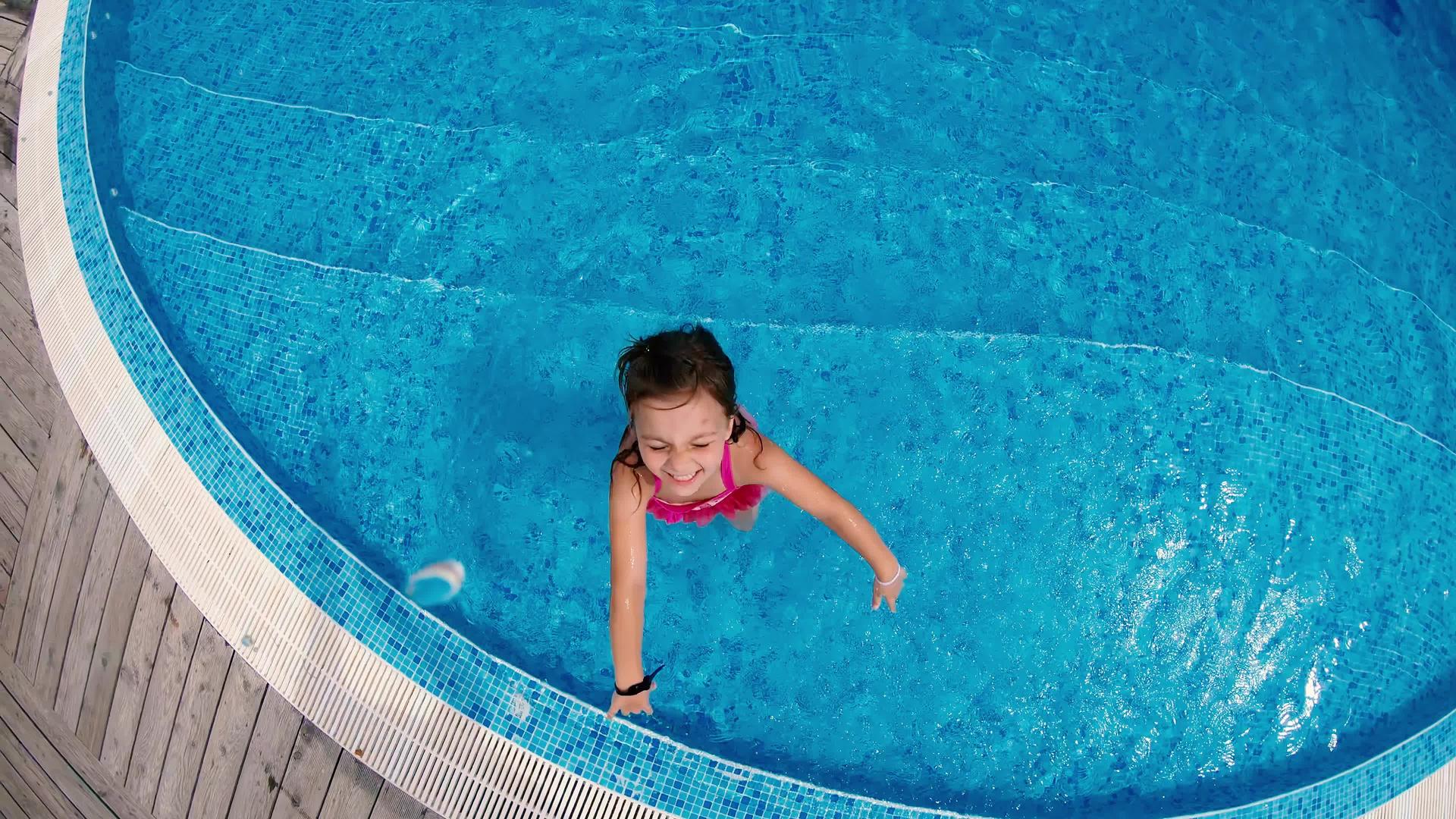 小女孩在游泳池里玩得很开心她站在游泳池里慢慢地看着相机视频的预览图