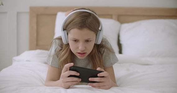 小女孩正在用智能手机玩网络游戏躺在卧室里用触摸屏视频的预览图