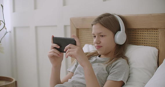 在校女生在智能手机上玩电子游戏通过互联网使用耳机并使用耳机视频的预览图