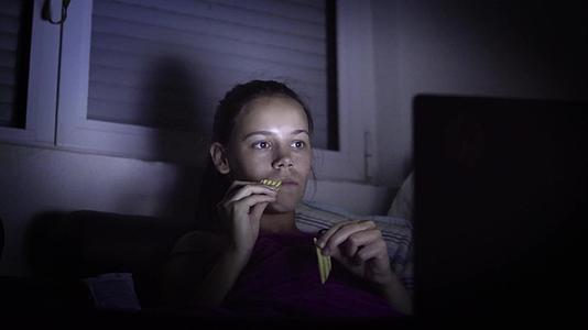 女孩在黑暗中看电视吃零食视频的预览图