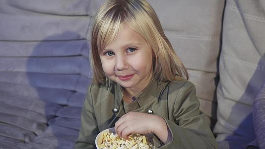 可爱的小女孩吃爆米花对着电影院的相机微笑视频的预览图