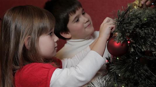 小男孩把装饰好的弓挂在圣诞树上视频的预览图