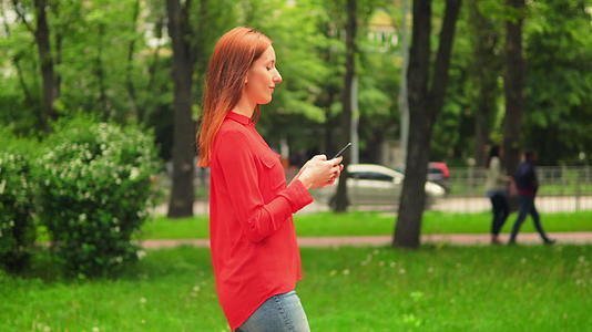 女孩走进绿色夏日公园发短信和短信视频的预览图