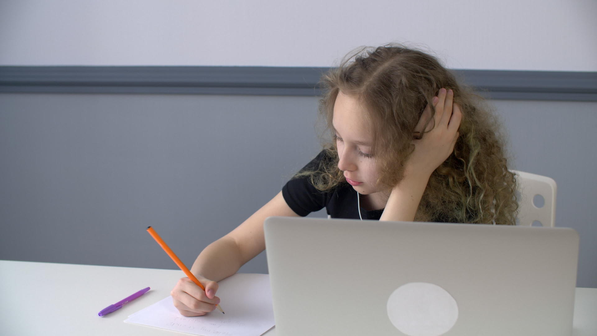 女孩和青少年在耳机前用铅笔在纸上写字视频的预览图