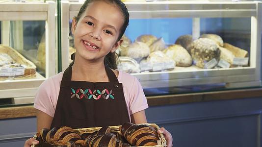 这个可爱的小女孩围裙在面包店工作对着镜头微笑视频的预览图