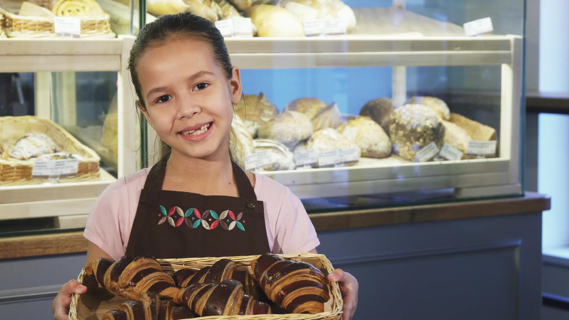 可爱的小女孩穿着围裙在面包店工作拿着一篮子蛋糕和蛋糕视频的预览图