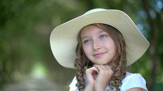 一个戴着白色帽子的可爱女孩的肖像在绿色花园里手牵手脸很可爱视频的预览图