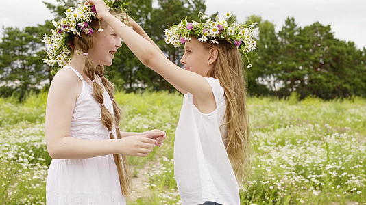 两个女孩戴着花环在夏天盛开的草地上快乐地玩耍视频的预览图