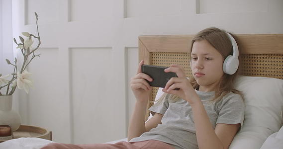 女学生躺在房间的床上通过互联网在智能手机上玩游戏视频的预览图