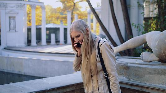 一个快乐的年轻女孩在城市秋季公园用手机在城市里说话视频的预览图