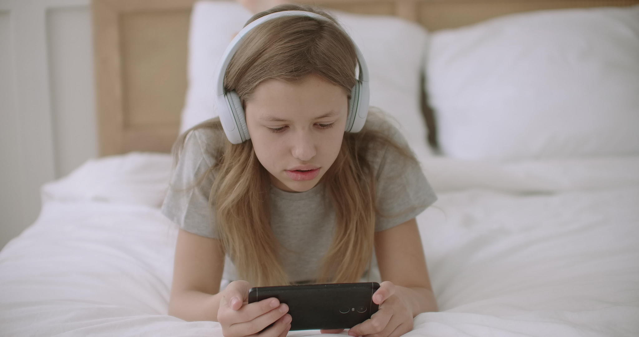 女孩躺在床上用无线耳机和无线耳机在手机屏幕上看文字Wifi视频的预览图