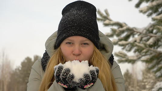 快乐的年轻女孩穿着冬衣双手吹雪视频的预览图