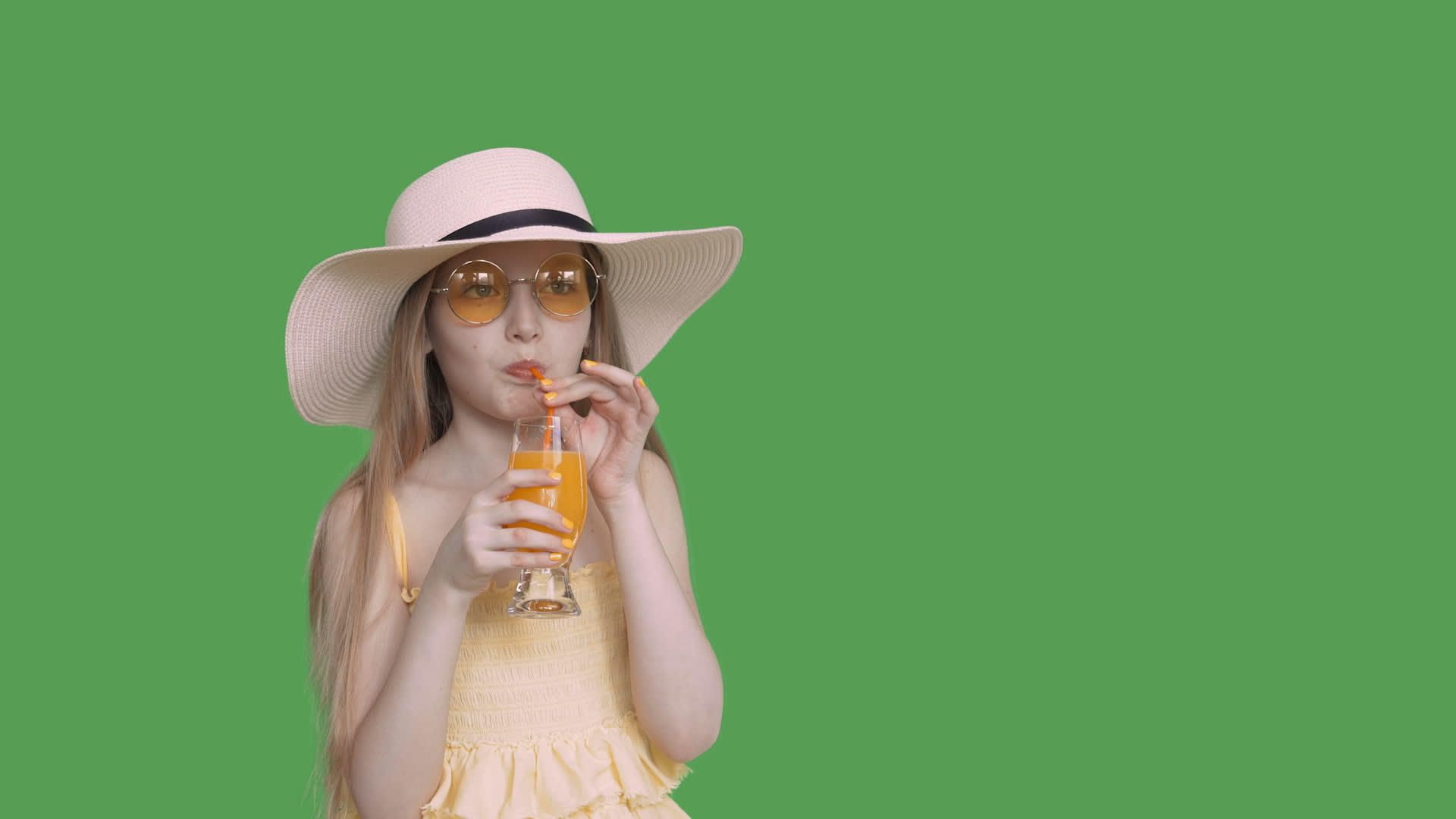 女孩从透明的绿色背景玻璃中用吸管喝橙汁戴上黄色的黄色视频的预览图