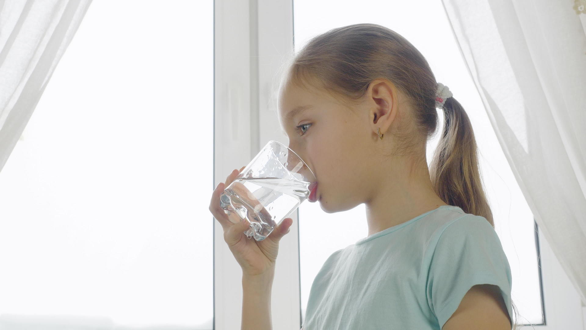 在家庭厨房窗户背景的玻璃杯中女孩和女孩的饮用水以窗户为背景视频的预览图