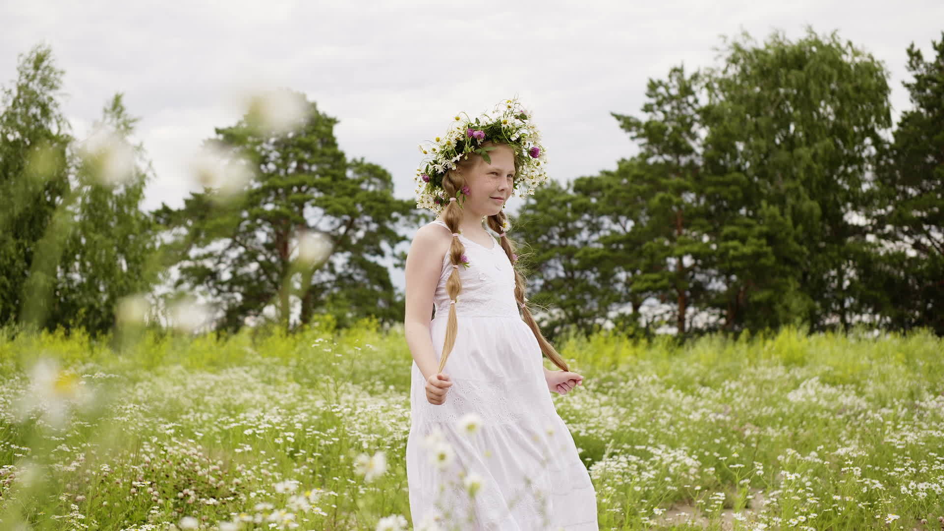 穿着花环和白裙子的女孩在花草地上安装了相机视频的预览图