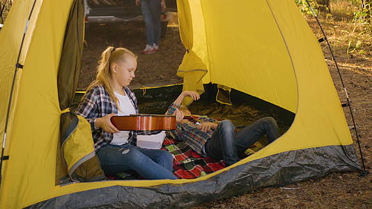 十几岁的女孩从露营帐篷里的男孩手里拿吉他十几岁的女孩视频的预览图