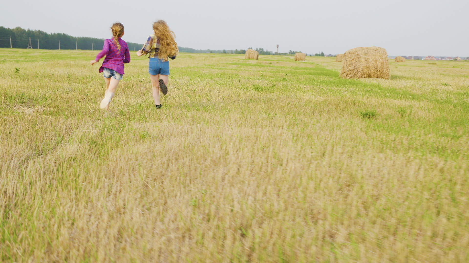 两个女孩少年在以干草堆为背景的乡村田野里奔跑视频的预览图