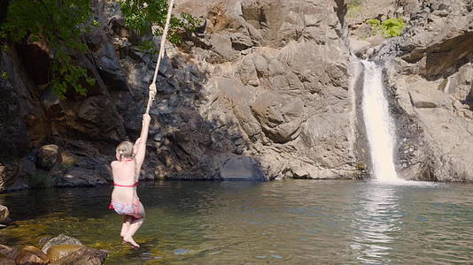 在流动的瀑布景观中女孩和少年从蹦极跳进山区的河流视频的预览图