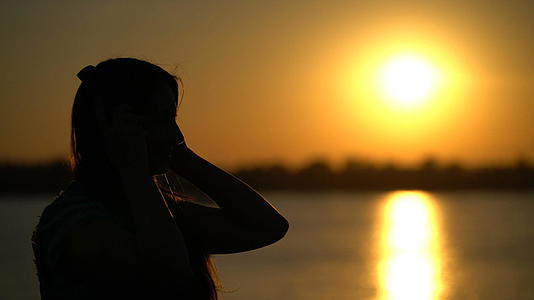 女性在日落背景下用耳机听音乐视频的预览图
