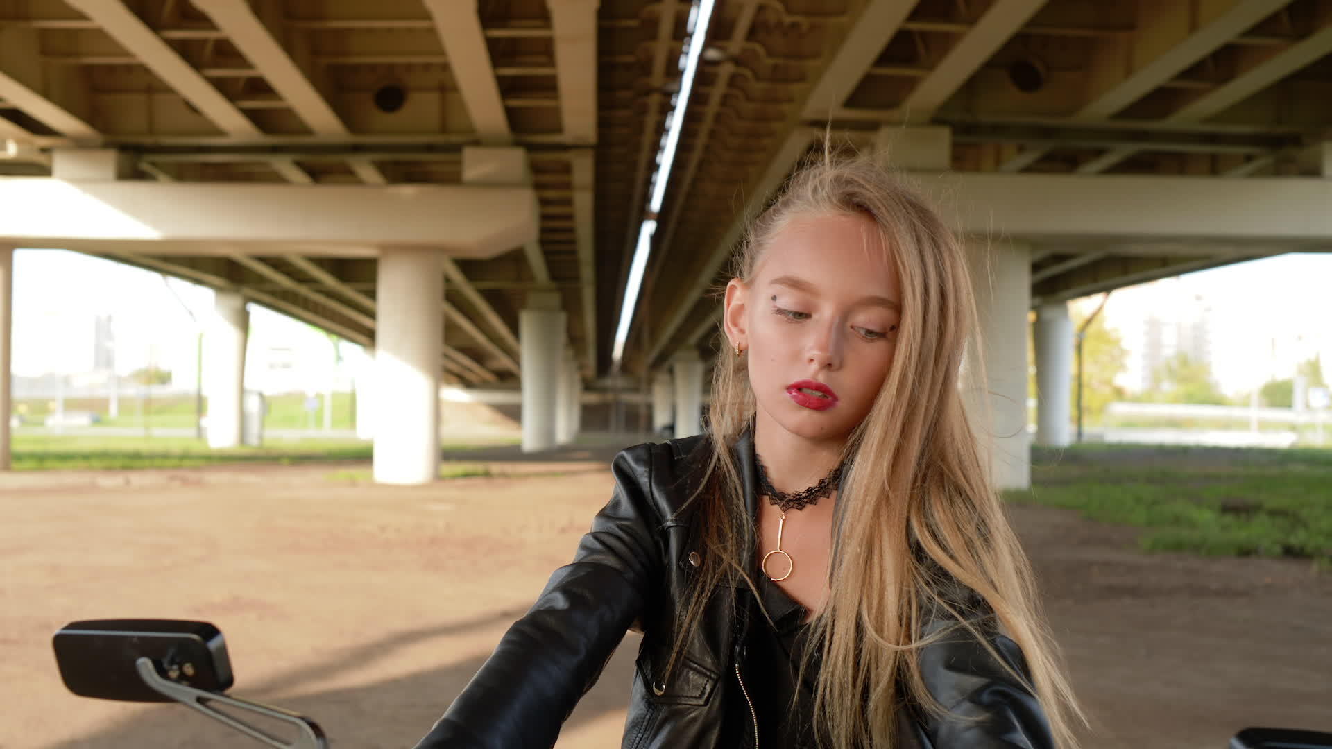 骑自行车的黑色皮夹克的女孩坐在汽车桥下的摩托车上视频的预览图