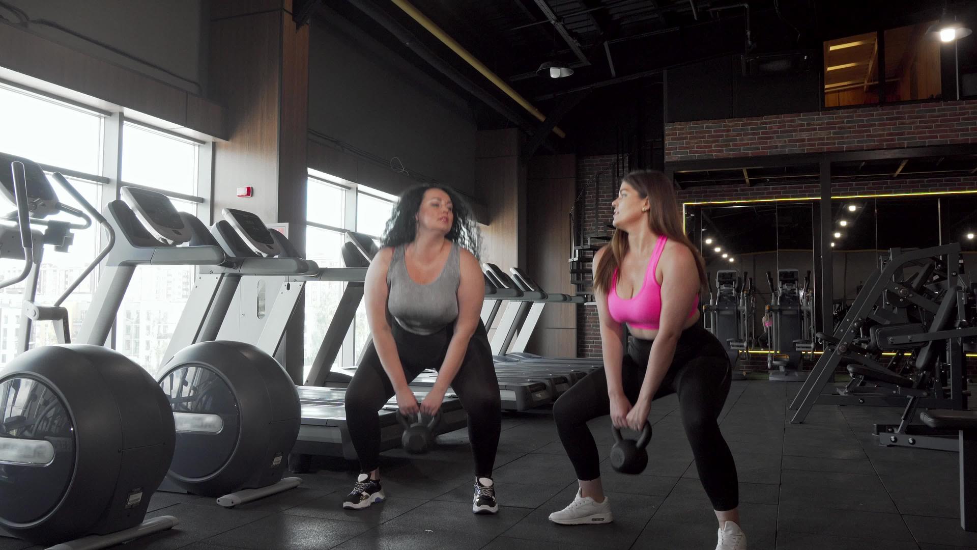 两位可爱、大、漂亮的女运动员坐在健身房里手里拿着小叮当视频的预览图