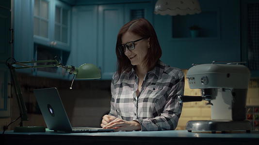 30多岁的年轻女性晚上戴着眼镜在蓝色厨房的家里用笔记本电脑视频的预览图