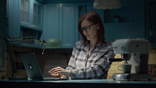 一位30多岁的年轻女子戴着眼镜在蓝色厨房的家里用笔记本电脑视频的预览图