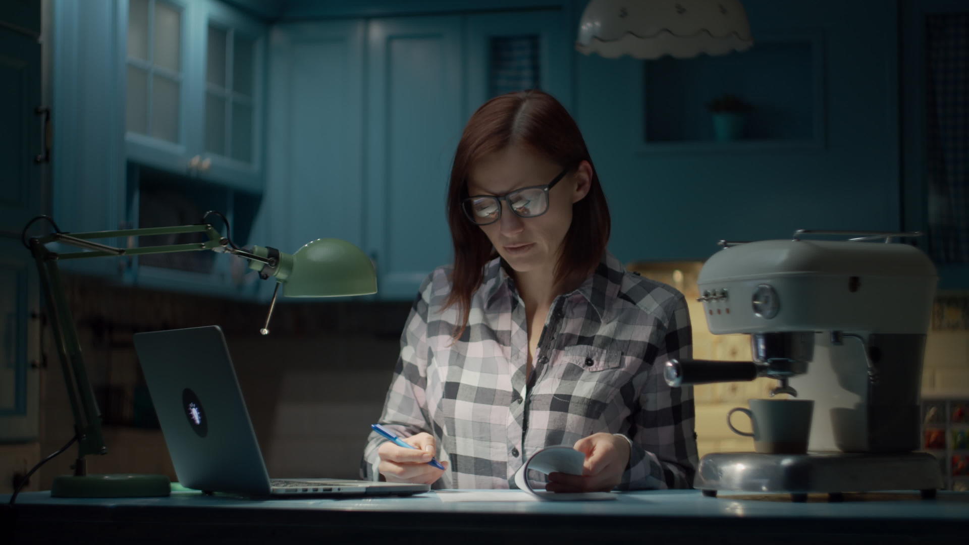 30多岁的年轻女性晚上戴着眼镜在蓝色厨房的家里用笔记本电脑视频的预览图