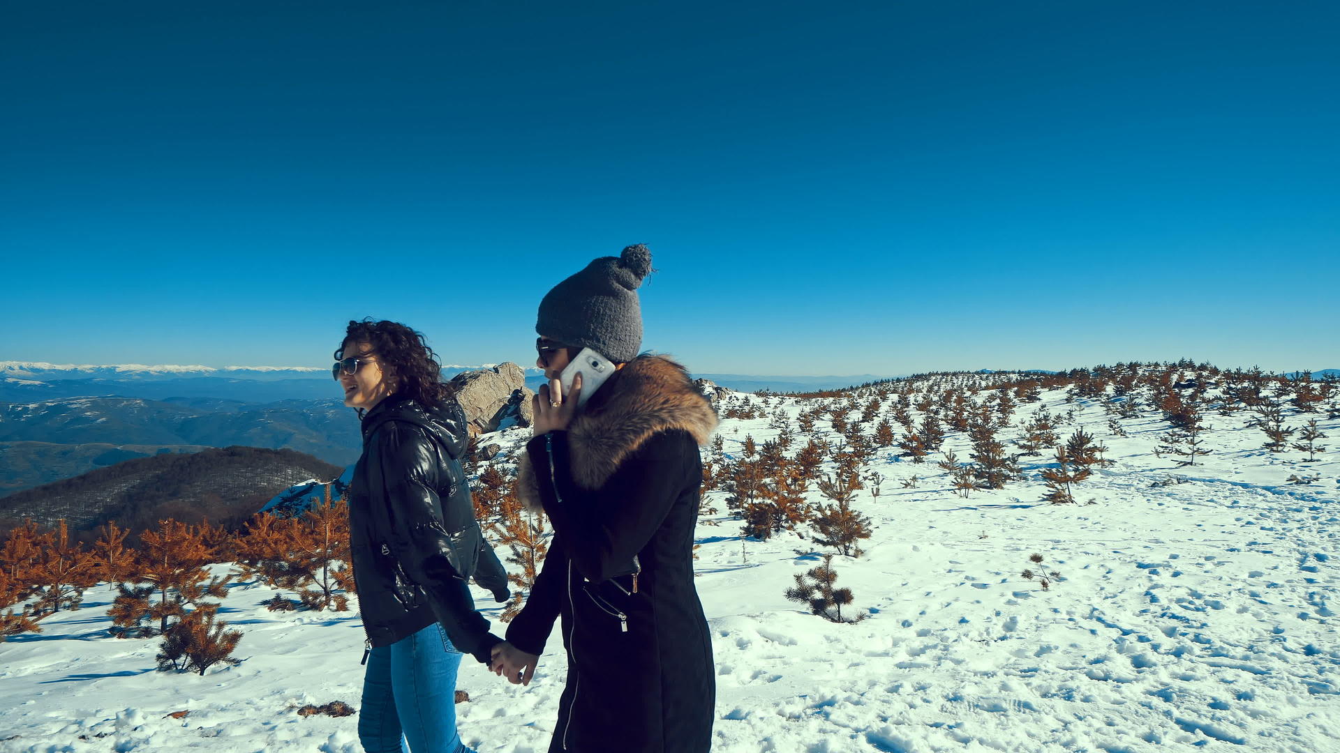两个女孩在雪地里走来走去手牵手微笑着用智能手机说话视频的预览图