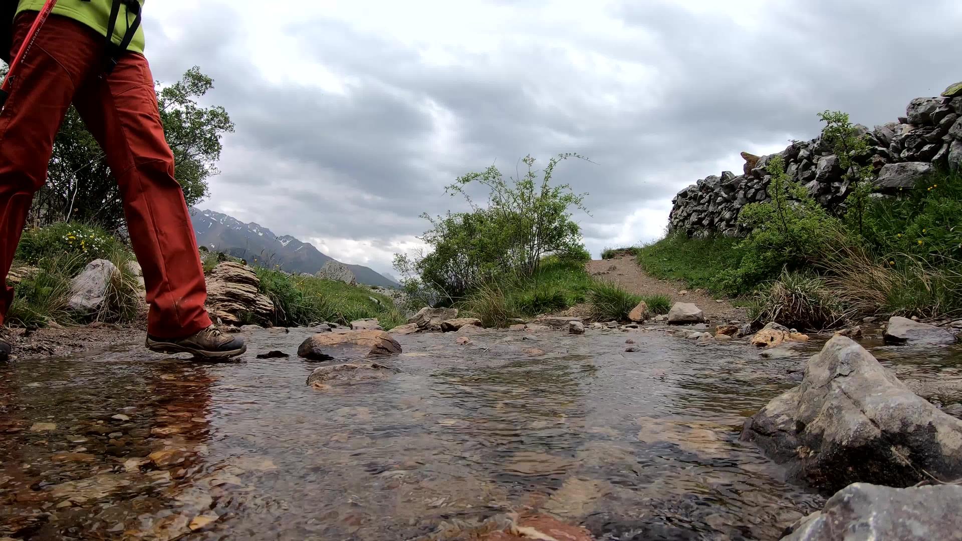 远足妇女穿过山上的小溪视频的预览图