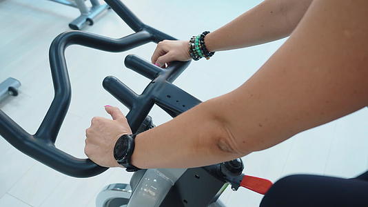 在体育俱乐部的自行车课上戴着健身手表的女性手里拿着一块房间视频的预览图
