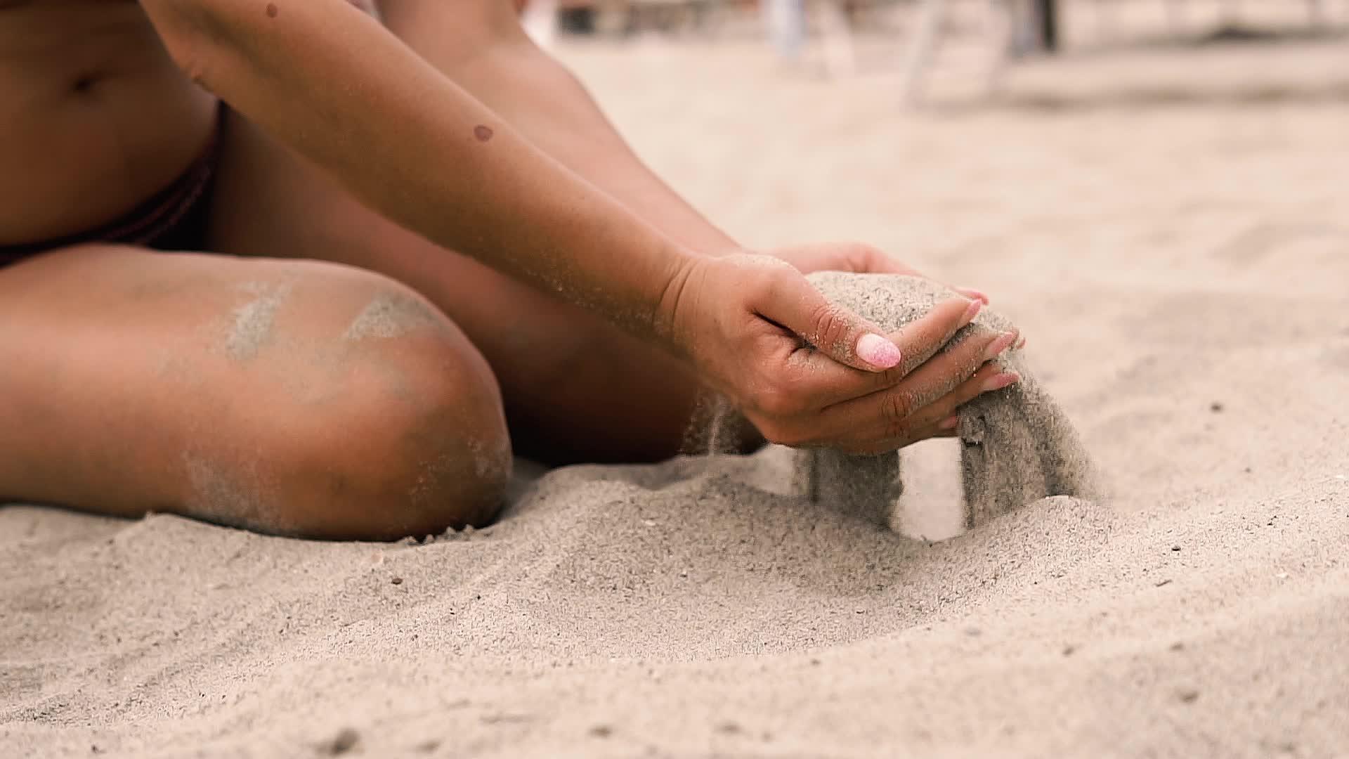 性感的女人在沙滩上的手指上慢慢地撒沙子视频的预览图