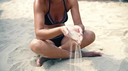 性感的女人在沙滩上的手指上慢慢地撒沙子视频的预览图