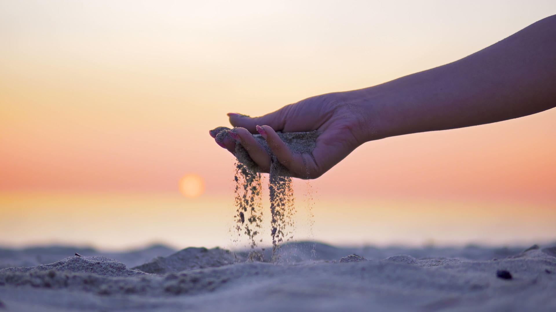 一个年轻女孩的手从海滩上向日落倾斜黄天倾泻沙子视频的预览图