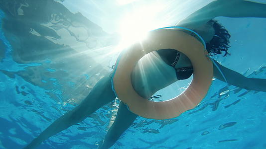 一个迷人的女人在阳光明媚的天气里漂浮在游泳池里视频的预览图