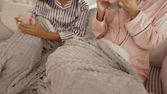 在室内场景中两位年轻美女用毯子在沙发上喝茶聊天——混血儿视频的预览图