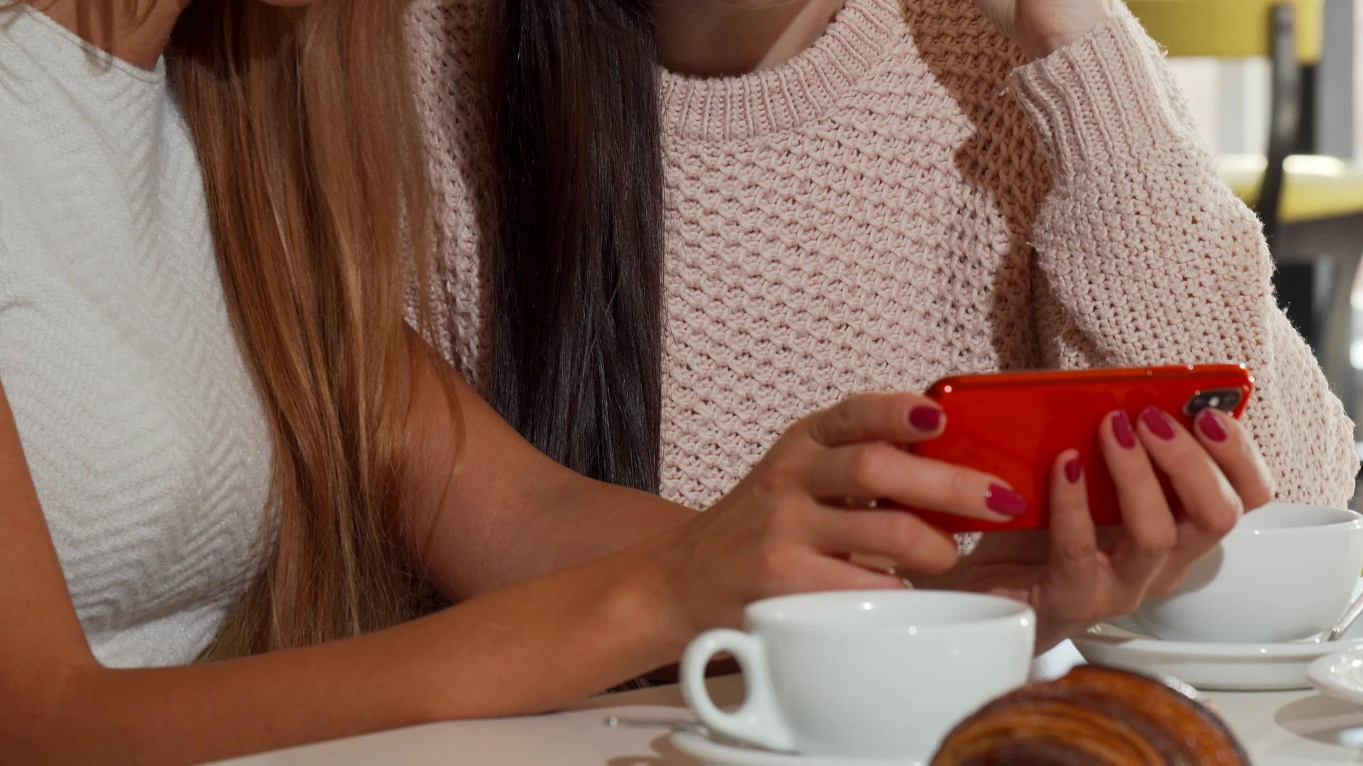 美丽的女性朋友和女同学一起在咖啡店使用智能手机视频的预览图
