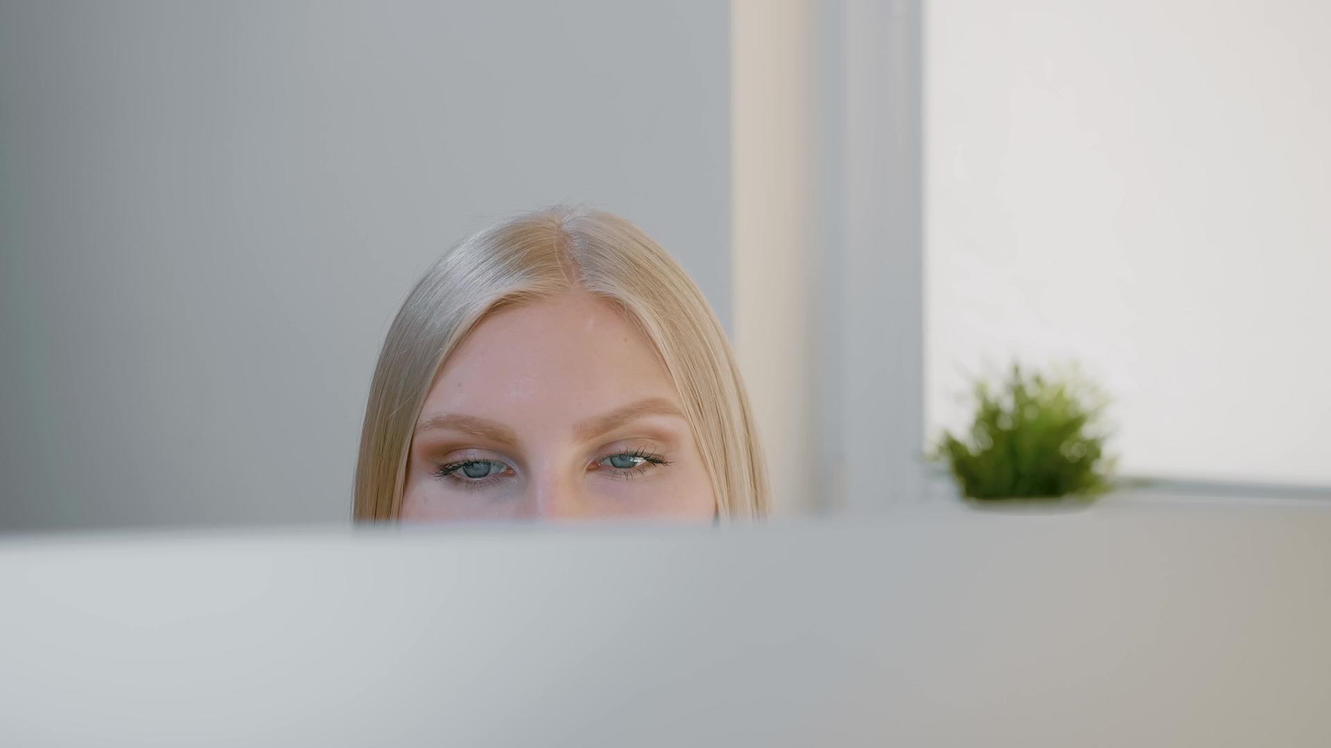 看着电脑显示器的女性金发美女坐在窗前专心地看着电脑屏幕视频的预览图