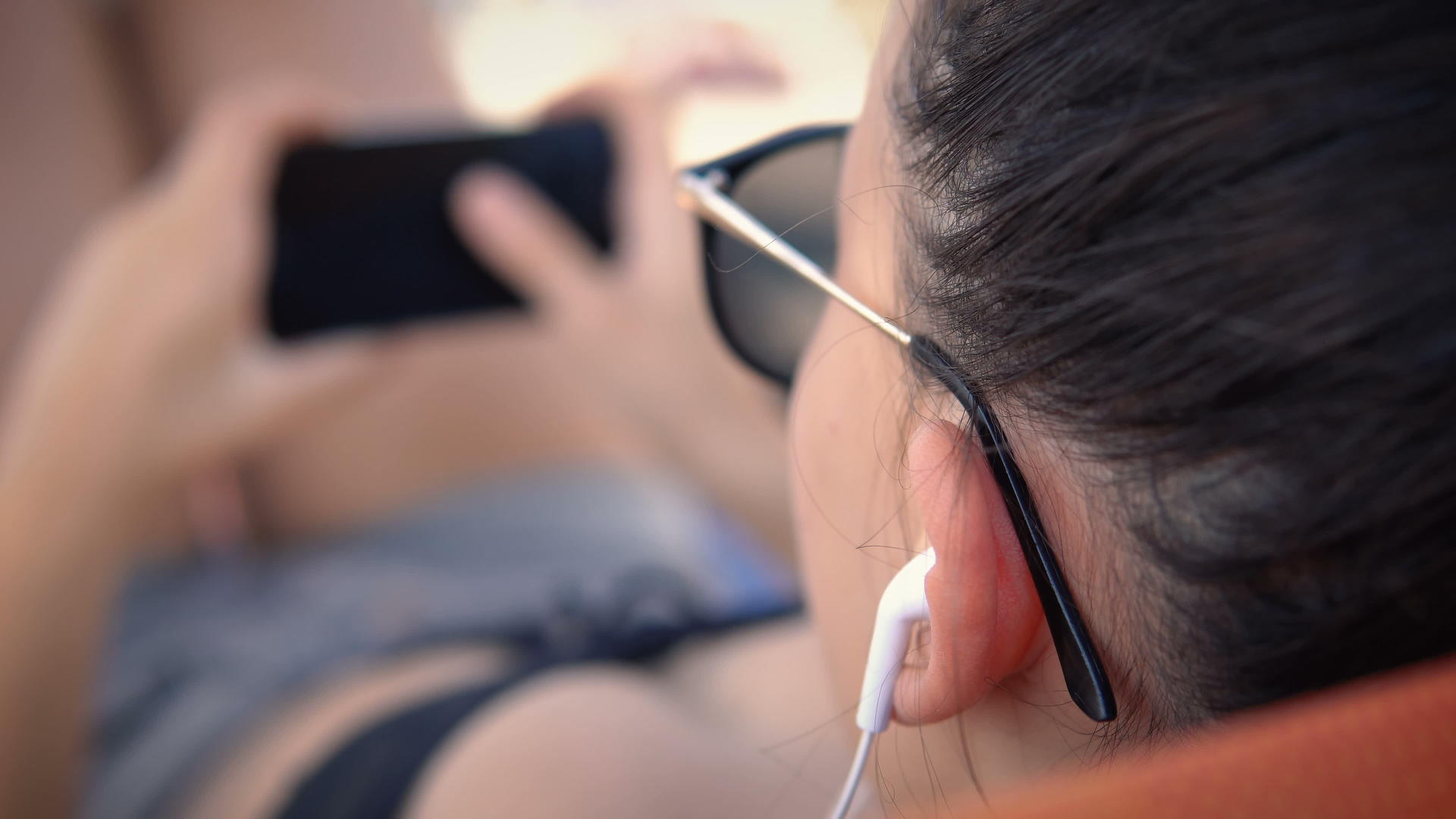 坐在海滩床上的女青少年在智能手机耳机上听音乐视频的预览图