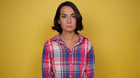 迷人的女人在黄色背景的格子衬衫和深色头发中表达粗心视频的预览图