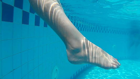 度假酒店透明游泳池水中的女性腿水下视图女性在蓝色水中视频的预览图