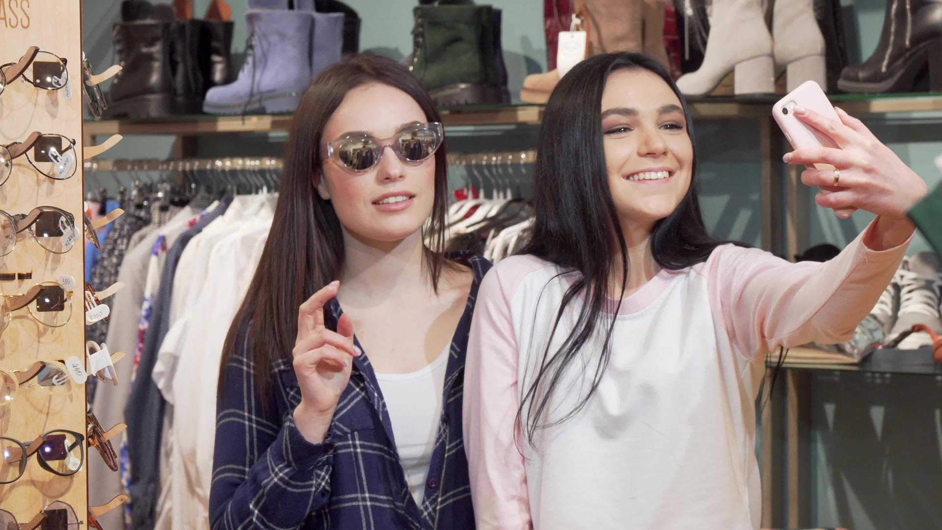 快乐的女性朋友在服装店用智能手机自拍视频的预览图