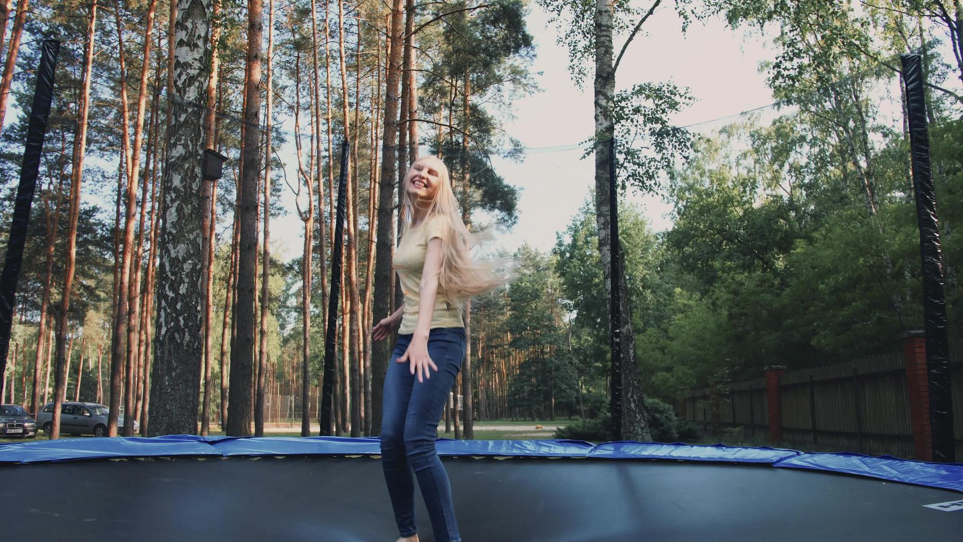 快乐的女人在蹦床上跳着美丽的年轻金发和赤脚女人穿着轻便的衣服视频的预览图