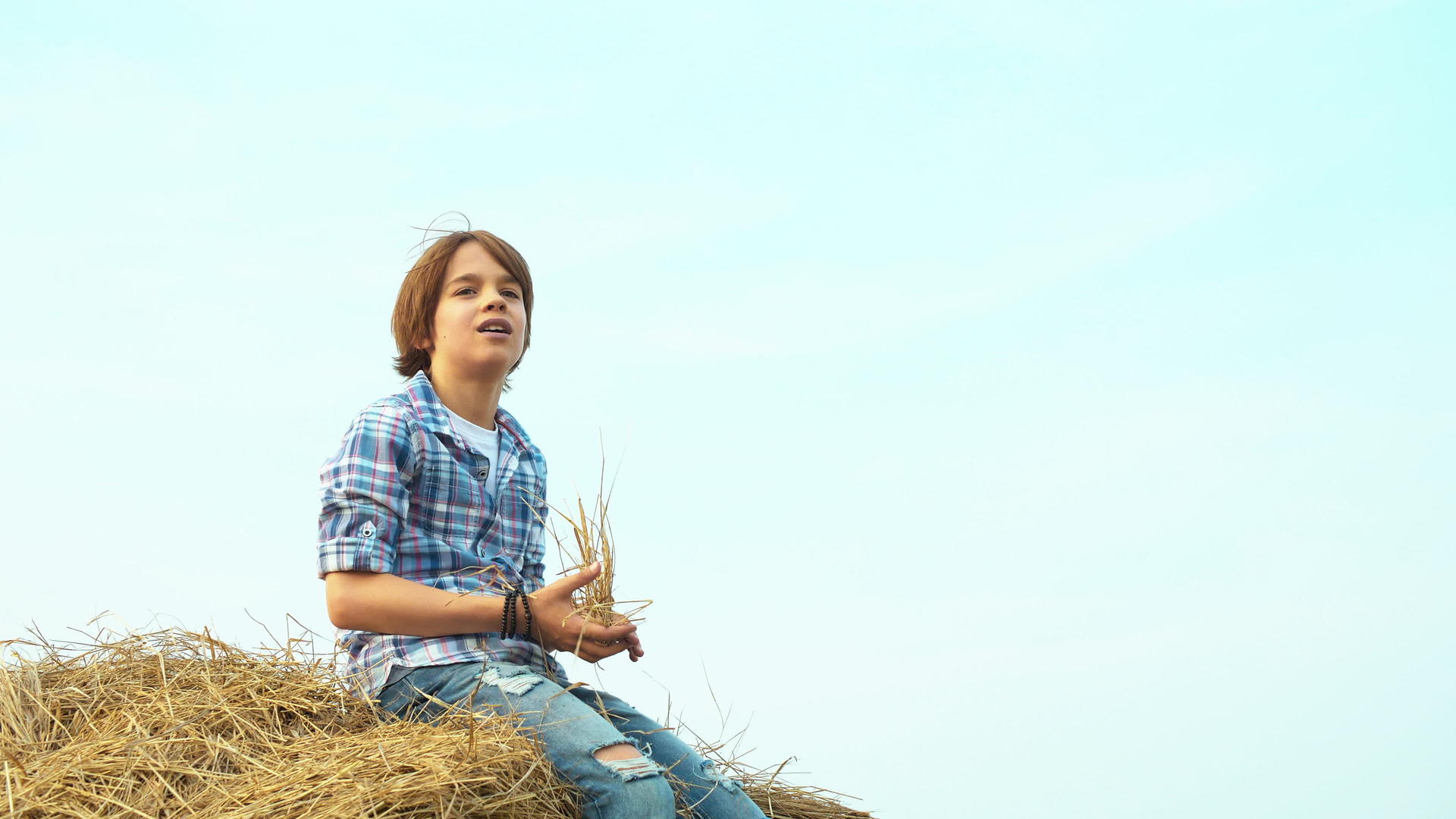 小男孩坐在村里收割场的干草堆上尖叫的小男孩坐在那里视频的预览图